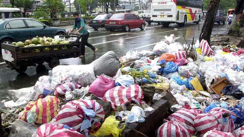 A coconut vendor partly covers his face as he passes by a mound of rubbish in Manila's Pasay district on Feb. 4, 2001. (Joel Nito/AFP/Getty Images)