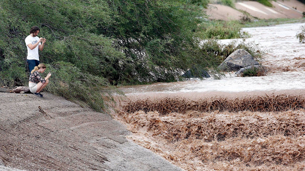 Thomas Ingersoll and Sydney Cisco watch flash flood waters from the Sonoran Desert overrun Skunk Creek, Tuesday, Aug. 19, 2014, in northwestern Phoenix. (AP Photo/Matt York)