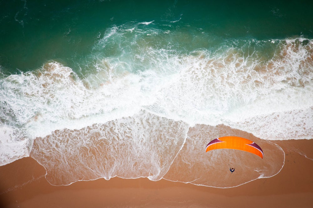 The turquoise waters of the Indian Ocean wash ashore as a paraglider hangs above. (Image: Jody MacDonald)