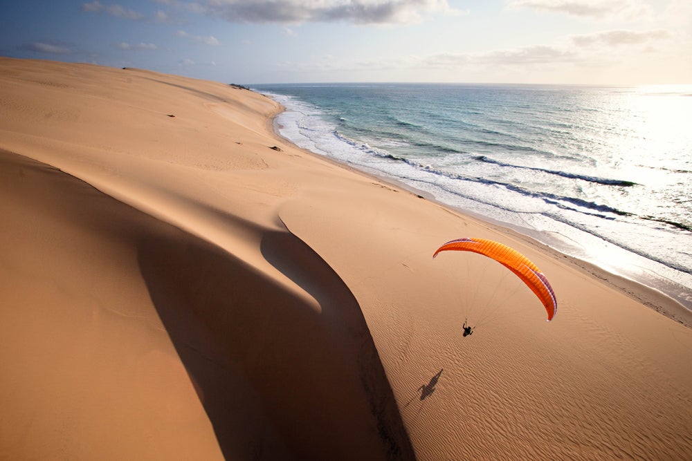 A gorgeous shot of a paraglider flying over the large sand dune near the shore. (Image: Jody MacDonald)