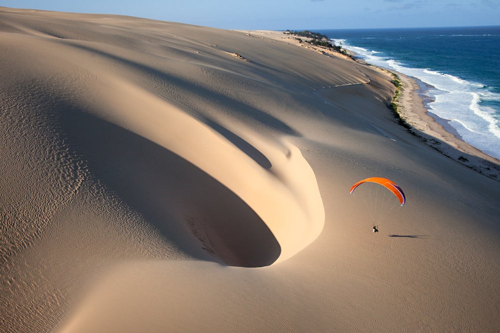 A paraglider flies along a large sand dune in the Bazaruto Archipelago in Mozambique. (Image: Jody MacDonald)