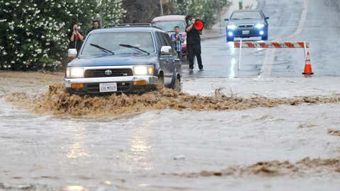 A vehicle drives through a flooded section of the road that was closed off on Pebble Beach Drive in Victorville, California, Sunday, July 19, 2015. (David Pardo/The Victor Valley Daily Press via AP)