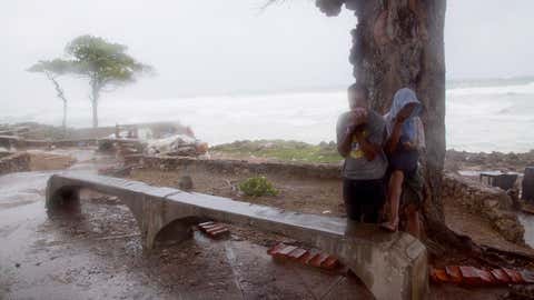 A couple of persons take refuge behind a tree against the strong winds of Tropical Storm Erika,as it approaches Santo Domingo,in the Dominican Republic,Friday,August 28,2015. Tropical Storm Erika began to lose steam Friday over the Dominican Republic,but it left behind a trail of destruction that included several people killed on the small eastern Caribbean island of Dominica,authorities said. (AP Photo/Tatiana Fernandez)