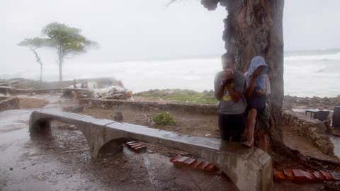 A couple of persons take refuge behind a tree against the strong winds of Tropical Storm Erika, as it approaches Santo Domingo, in the Dominican Republic, Friday, August 28, 2015. Tropical Storm Erika began to lose steam Friday over the Dominican Republic, but it left behind a trail of destruction that included several people killed on the small eastern Caribbean island of Dominica, authorities said. (AP Photo/Tatiana Fernandez)