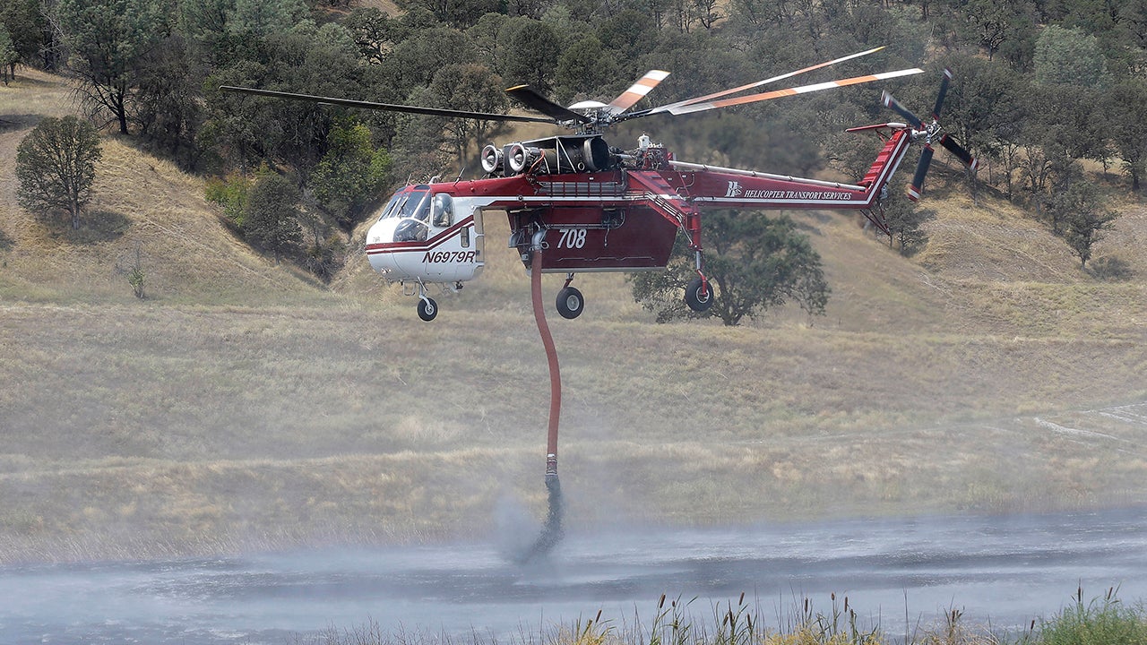 A helicopter pilot takes water from a pond near Clearlake, Calif., Wednesday, Aug. 5, 2015. Thousands of firefighters battling an unruly Northern California wildfire were aided overnight by cooler temperatures and higher humidity, but the fire is still less than a quarter contained. (AP Photo/Jeff Chiu)