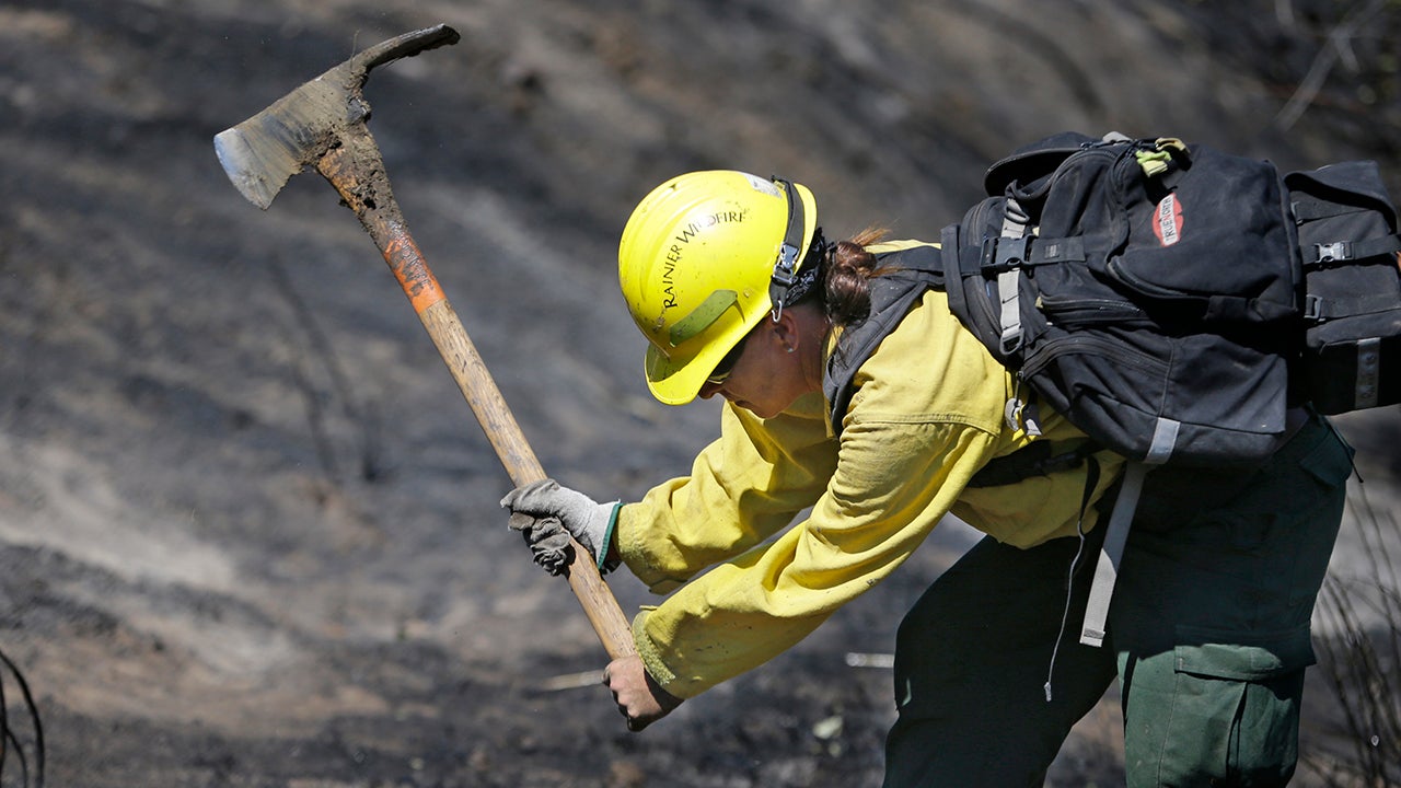 Firefighter Kelly Willman works to put out still smoldering hot spots from a wildfire two days earlier, Tuesday, June 30, 2015, in Wenatchee, Wash. Two dozen homes were destroyed in a fast-moving wildfire Sunday night in Wenatchee,. A handful of businesses also were destroyed when flames spread to the downtown core. (AP Photo/Elaine Thompson)