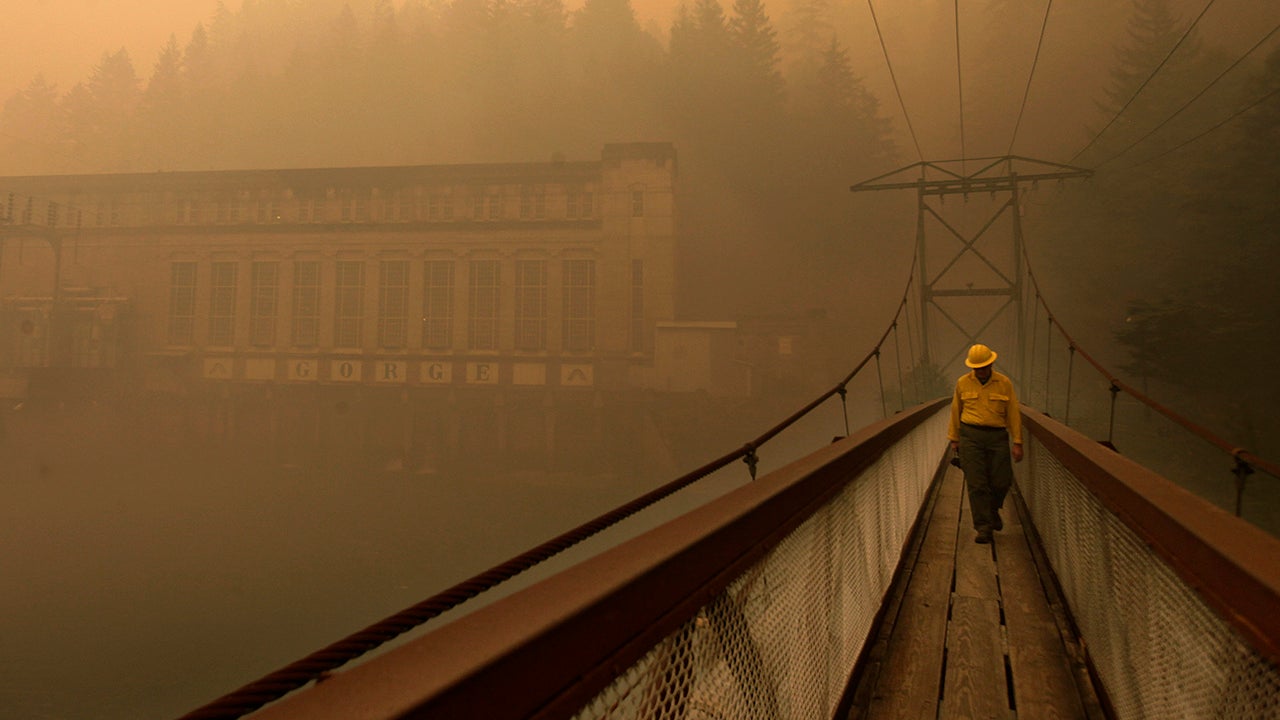 Dennis Godfrey, with the Great Basin Incident Management Team 4, walks across a bridge from the Gorge Powerhouse, Wednesday, Aug. 26, 2015, near Newhalem, Wash. Smoky conditions grounded helicopters and airplanes Wednesday that had been fighting the fires. (Mark Mulligan/The Herald/AP)