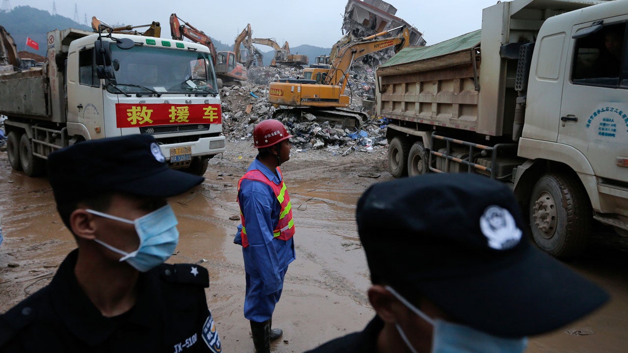 Policemen stand guard as excavators dig the rubble during a search operation for potential survivors near a damaged buildings following a landslide at an industrial park in Shenzhen, in south China's Guangdong province, Tuesday, Dec. 22, 2015. (AP Photo/Andy Wong)