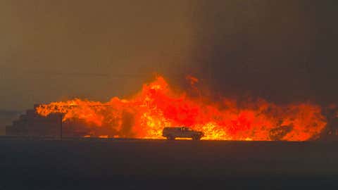 A Benton City Fire District 1 truck travels north on Hwy 125 in front of a flaming stack of hay bales near the intersection with Valley Grove Road north of Walla Walla, Washington, Sunday night, Aug. 21, 2016. (Greg Lehman/Walla Walla Union-Bulletin via AP)