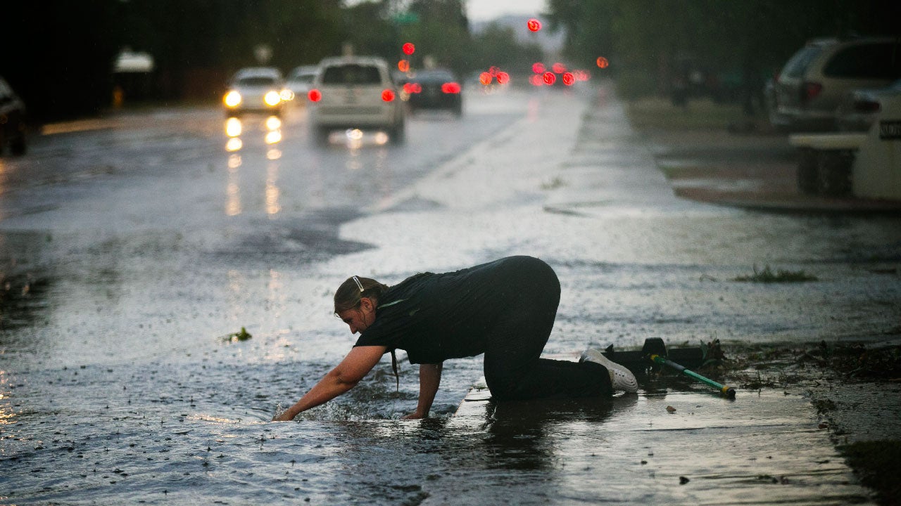 Silvia Graham removes debris from a storm drain in front of her home as 40th Street floods south of Thomas Road in Phoenix following heavy rains on Monday evening, July 18, 2016. (David Wallace/The Arizona Republic via AP)
