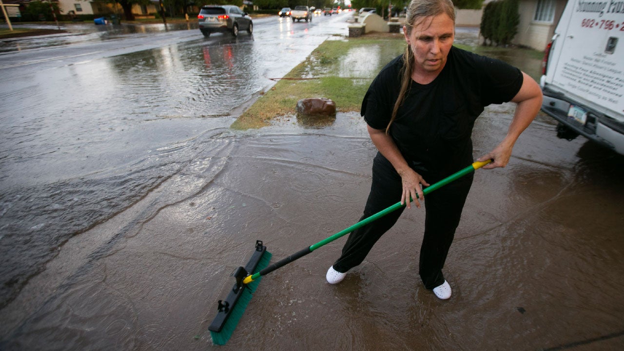 Silvia Graham sweeps water out of her driveway in front of her home as 40th Street floods south of Thomas Road in Phoenix following heavy rains on Monday evening, July 18, 2016. (David Wallace/The Arizona Republic via AP)