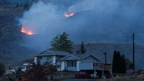 A wildfire burns on a mountain in the distance behind a house that remains standing on the Ashcroft First Nation, near Ashcroft, B.C., late Sunday July 9, 2017. As if the risk of losing their homes isn't enough, wildfire evacuees in British Columbia have faced the additional threat of looters searching through their belongings after they rushed to safety. THE CANADIAN PRESS/Darryl Dyck via 660News.com