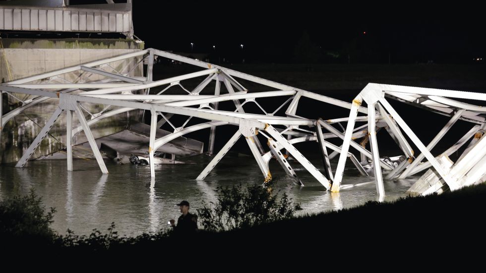 A police officer walks along the bank near the collapsed Interstate-5 bridge submerged after collapsing into the Skagit River, dumping vehicles and people into the water, in Mount Vernon, Wash., Thursday, May 23, 2013. (AP Photo/Elaine Thompson)