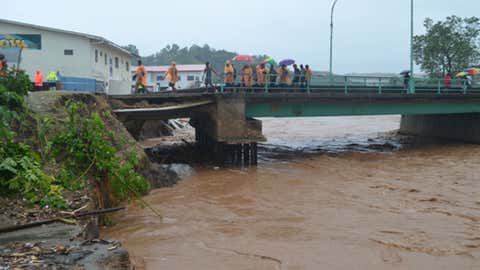 People with rain wear and umbrellas cross a bridge over the flooded Mataniko River in Honiara, Solomon Islands.(AP Photo/Solomon Star)