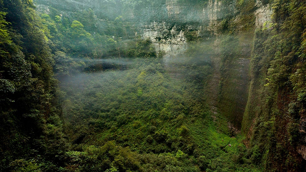 View from a small window in the wall of the vast Niubizi Tian Keng in the Er Wang Dong cave system. Cave explorers wander around the heavily vegetated floor. (Robbie Shone/Caters News Agency)