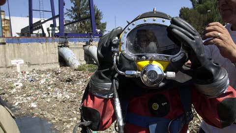 An assistant helps Ricardo, a diver, put on a helmet before he travels down to a drainage canal of polluted water April 11, 2002, in Mexico City, Mexico. (Susana Gonzalez/Getty Images)