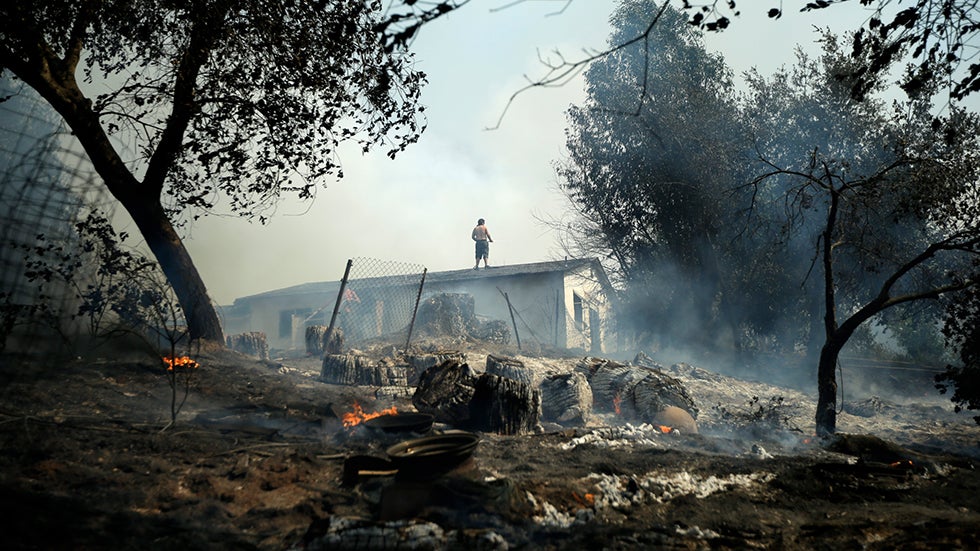 Jeff Brown waters the roof of his home as vegetation smolders during a wildfire, Thursday, May 15, 2014, in Escondido, Calif. (AP Photo/Gregory Bull)