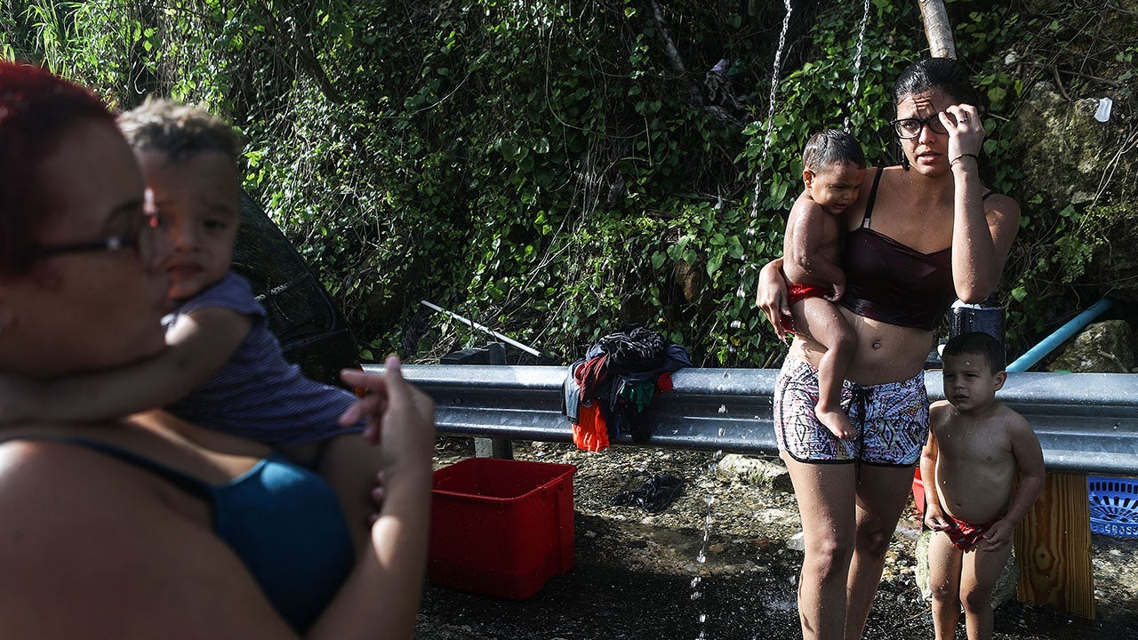 Mother Anais Rivera (right) stands with her three children as a friend (left) assists as they bathe and wash clothes with water funneled from a mountain stream, nearly one month after Hurricane Maria struck, on October 19, 2017 in Utuado, Puerto Rico. Rivera said they have no running water or electricity in their home and she visits the location to bathe, wash clothes and collect water for use at home. (Mario Tama/Getty Images)