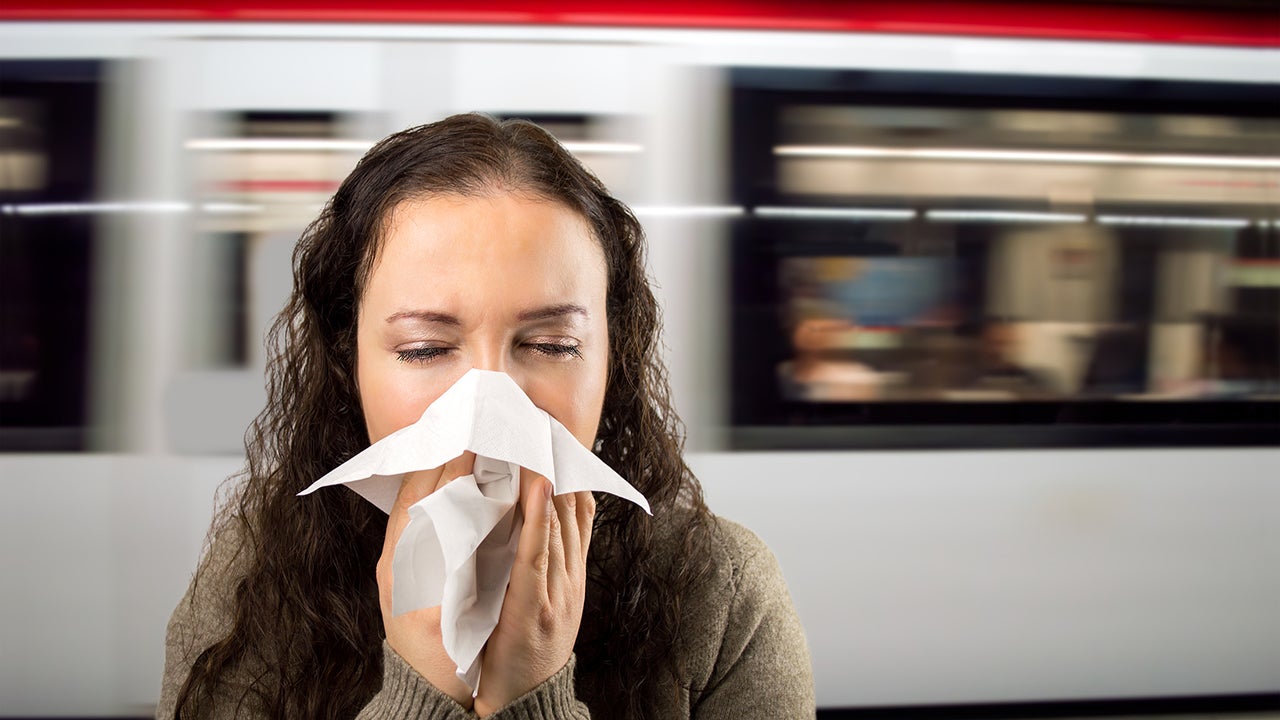 sneezing woman sick blowing nose at the subway station