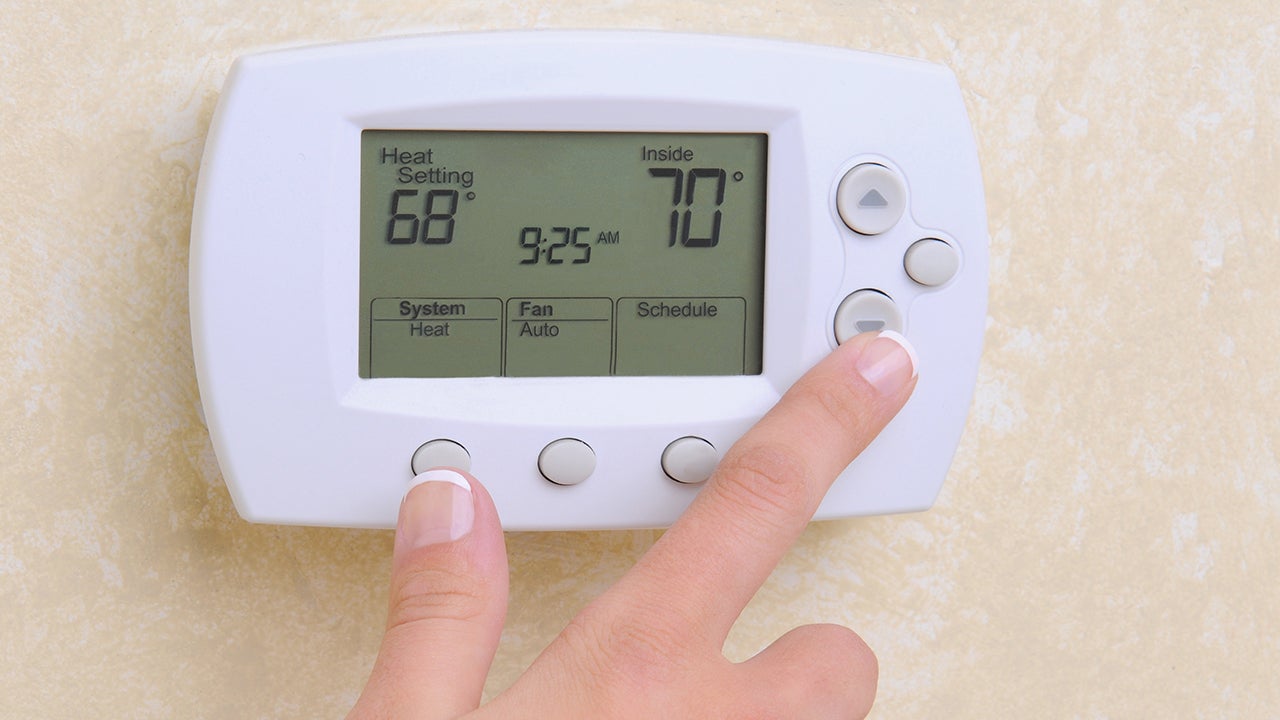 Closeup of a womans hand setting the room temperature on a modern programable thermostat.