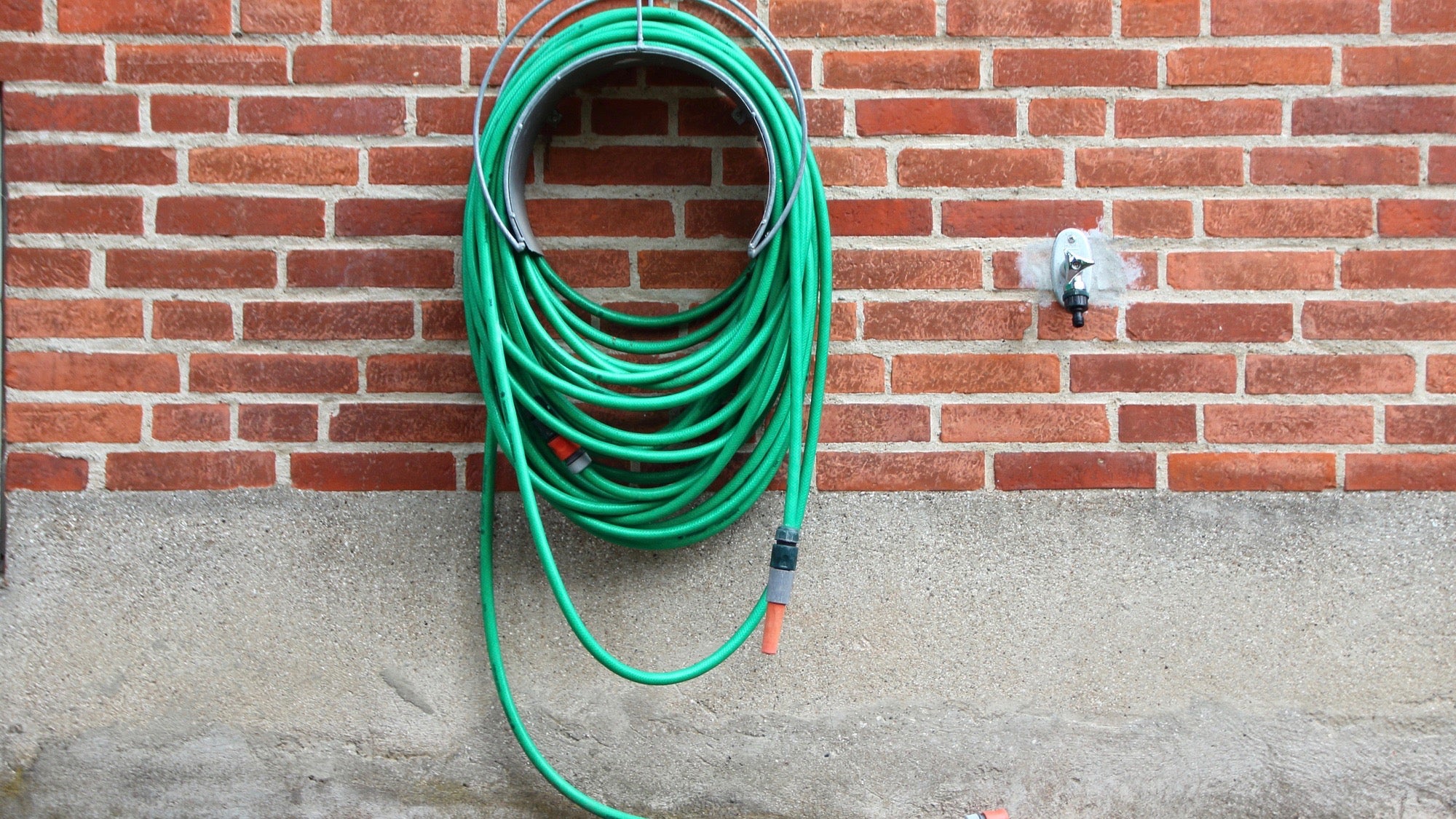 Green Garden Water Hose Hanging on Red Brickwall. Not connected to Water Tap.