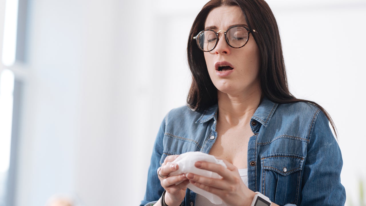 Cover your mouth. Attractive brunette keeping her eyes closed holding serviette in both hands, opening her mouth