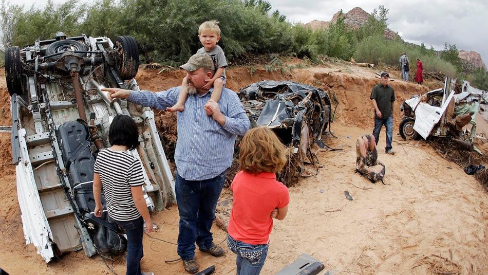 Russ Cook and his family stands next to severely damage vehicles swept away during a flash flood Tuesday, Sept. 15, 2015, in Hildale, Utah. Water swept away the vehicles in the Utah-Arizona border town, killing several people.