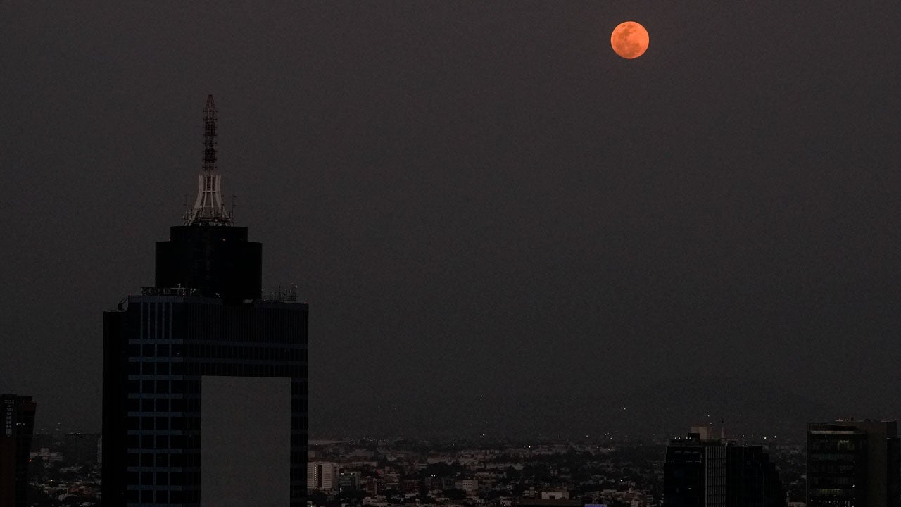 Red full moon rising over a city during a total lunar eclipse