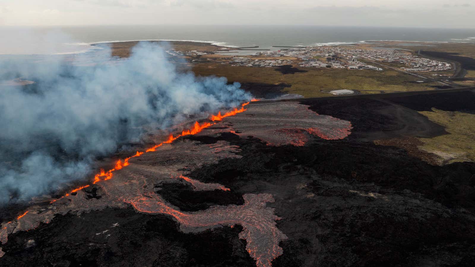 Reykjanes Peninsula A fissure of orange lava and white smoke is seen with a town in the background