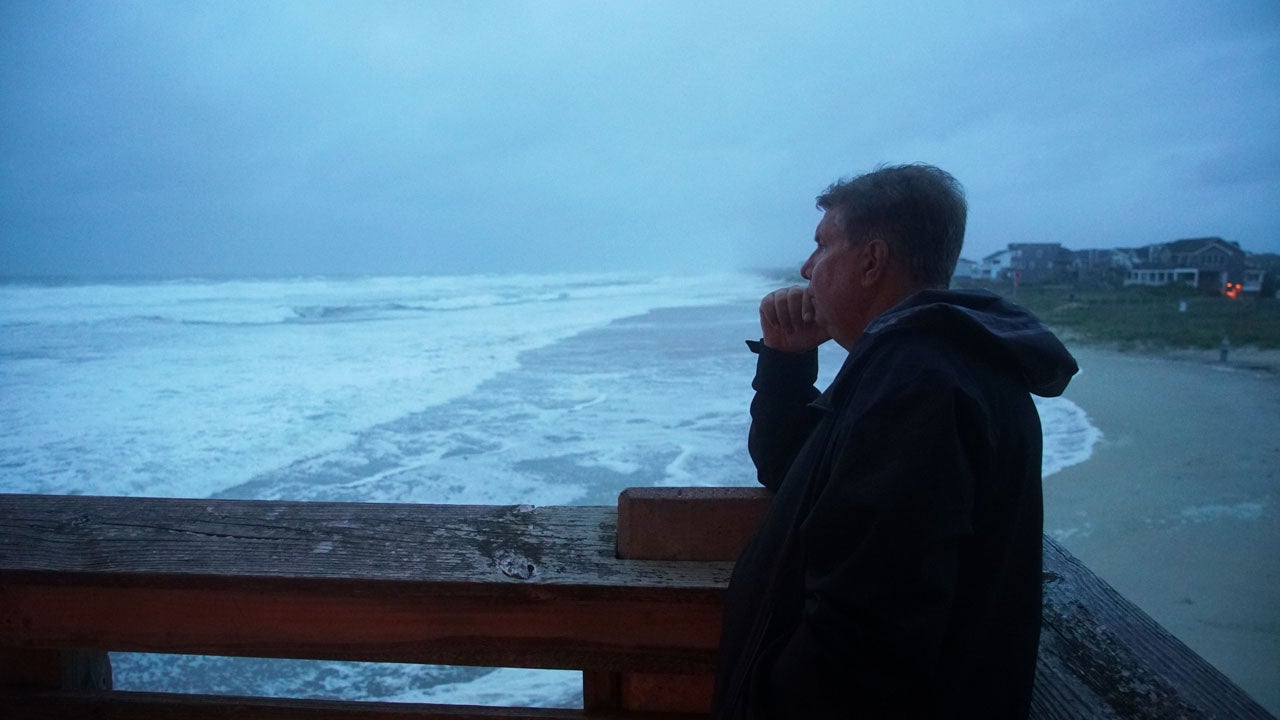 A man stands on a dock and looks out at the ocean during a hurricane