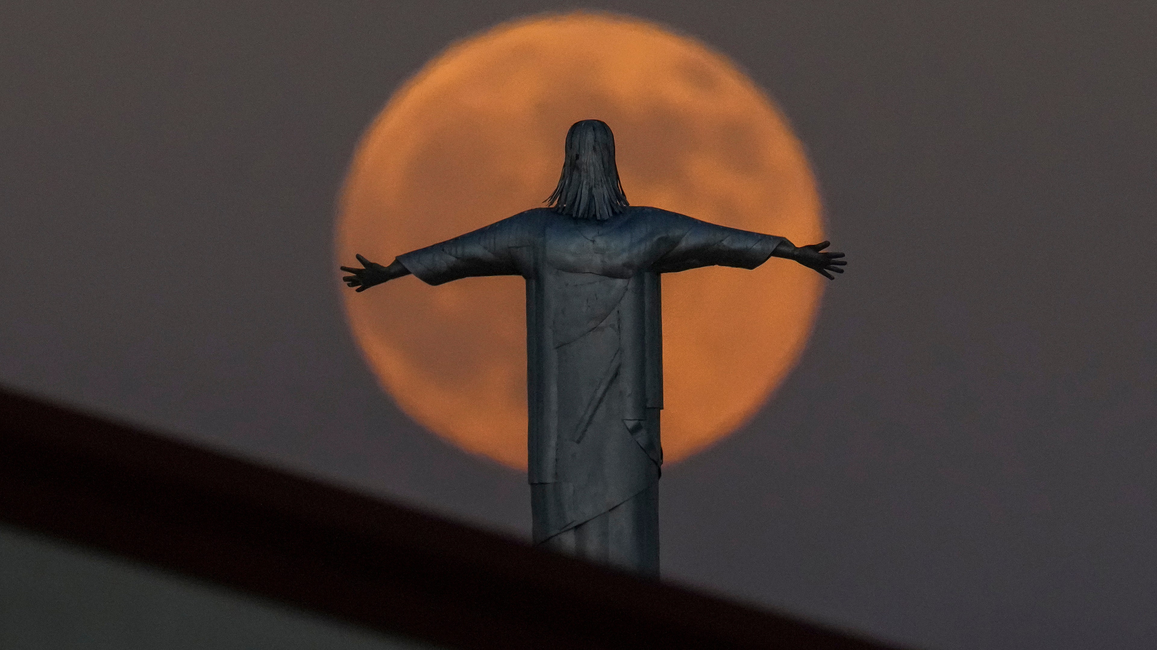 The harvest supermoon rises behind a statue of Jesus Christ at the top of Iglesia Luterana Santa Maria from Guadalupe to Irving, Texas.