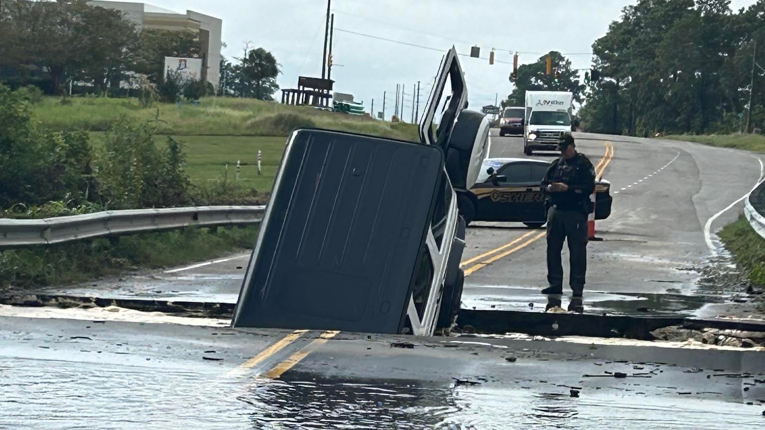 A car sits nose down in a section of washed out road.