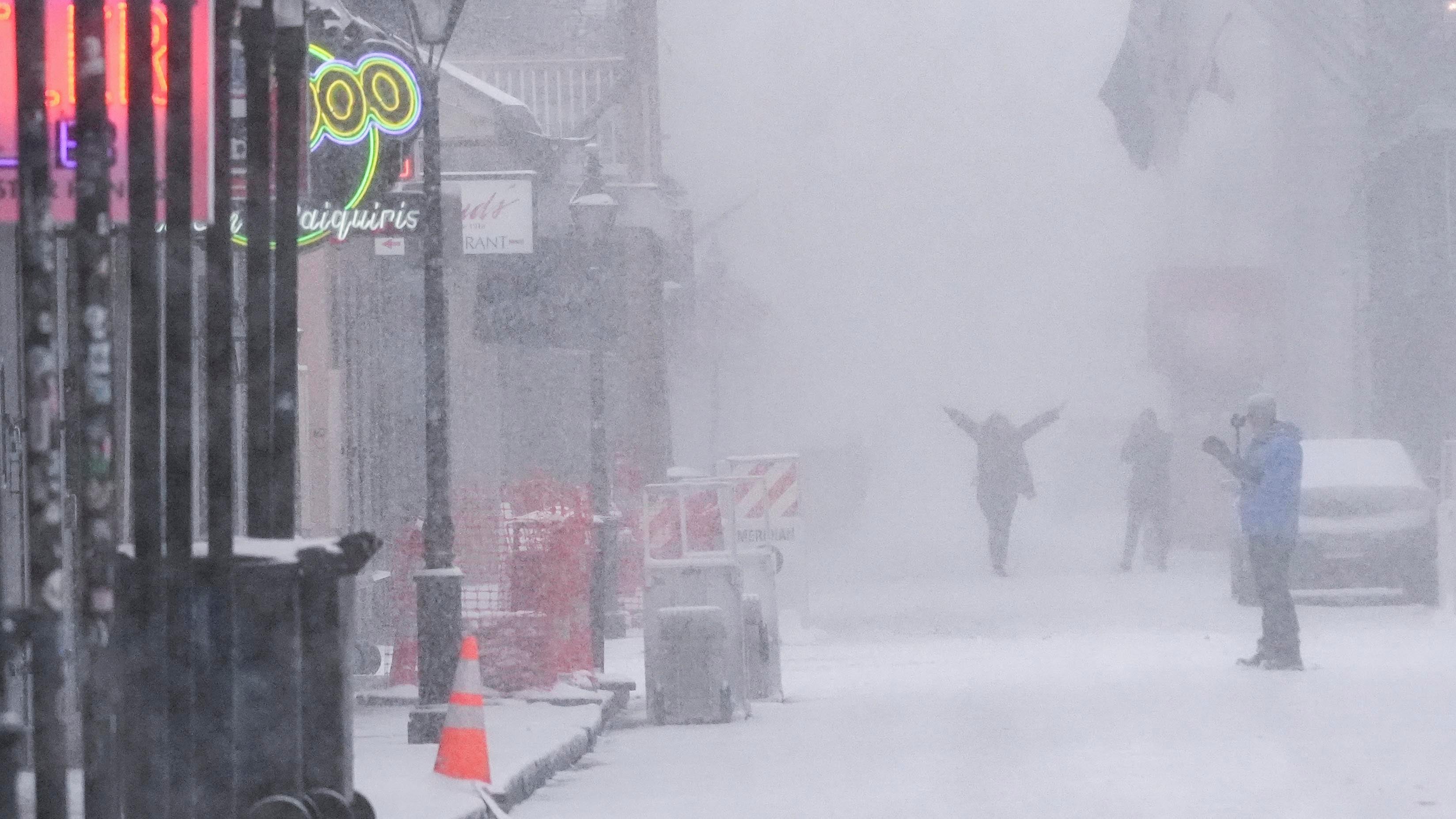 Two lone people walk on a snow-covered street, as more snow falls.
