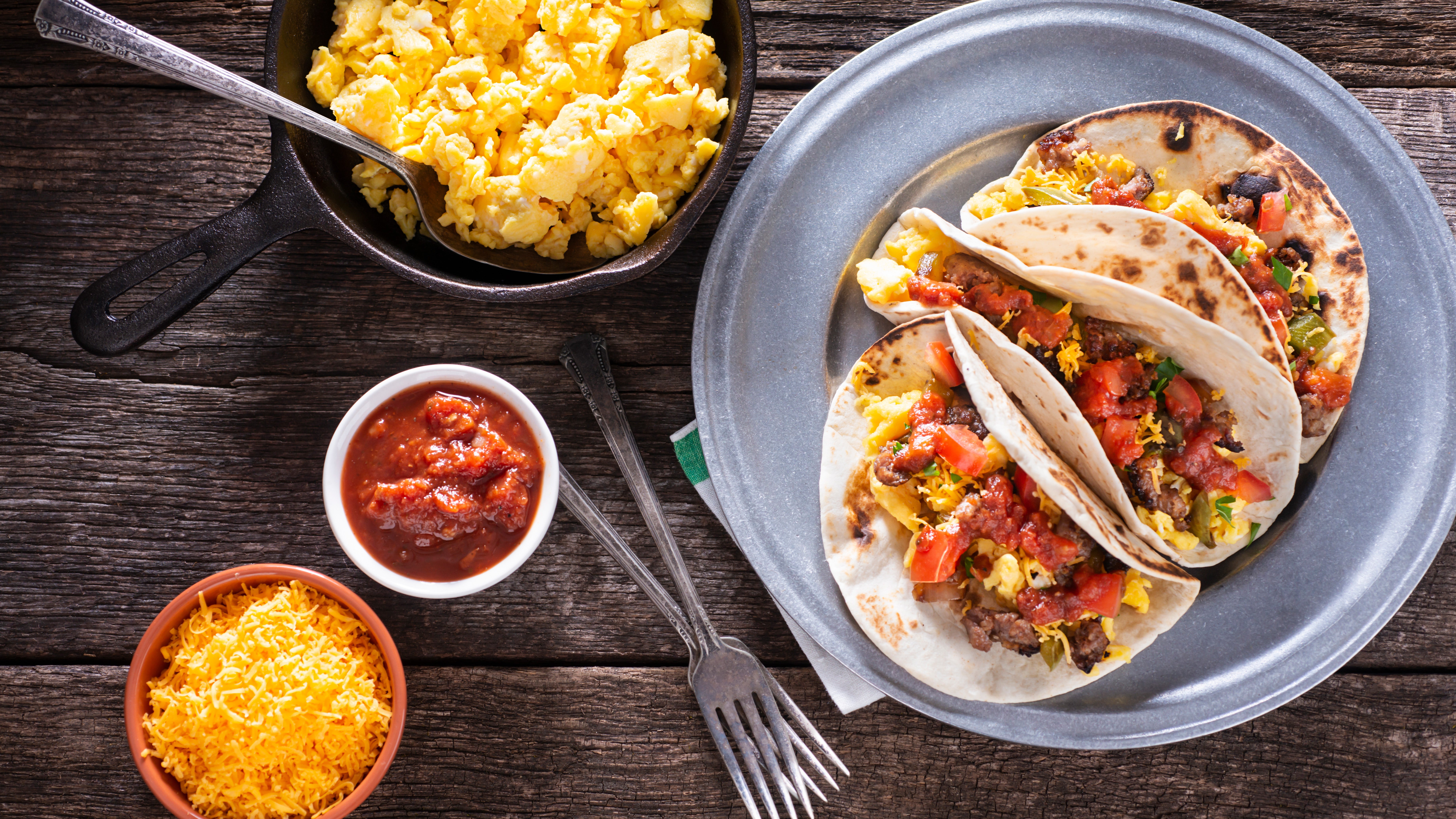 Tortillas filled with scrambled eggs sit on a silver plate, with cheese and salsa nearby.