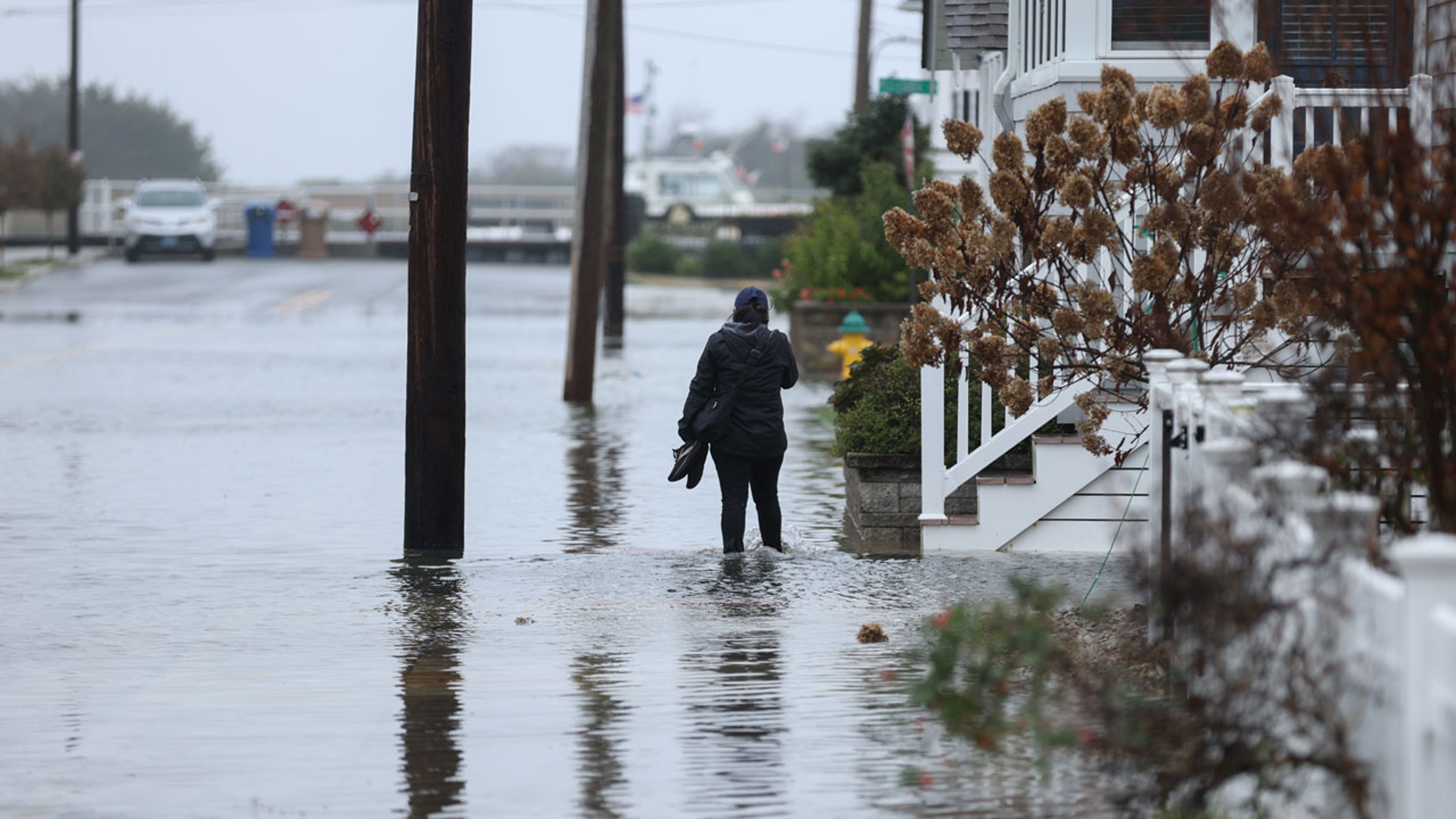 A person wearing a rain coat stands in knee-deep floodwaters