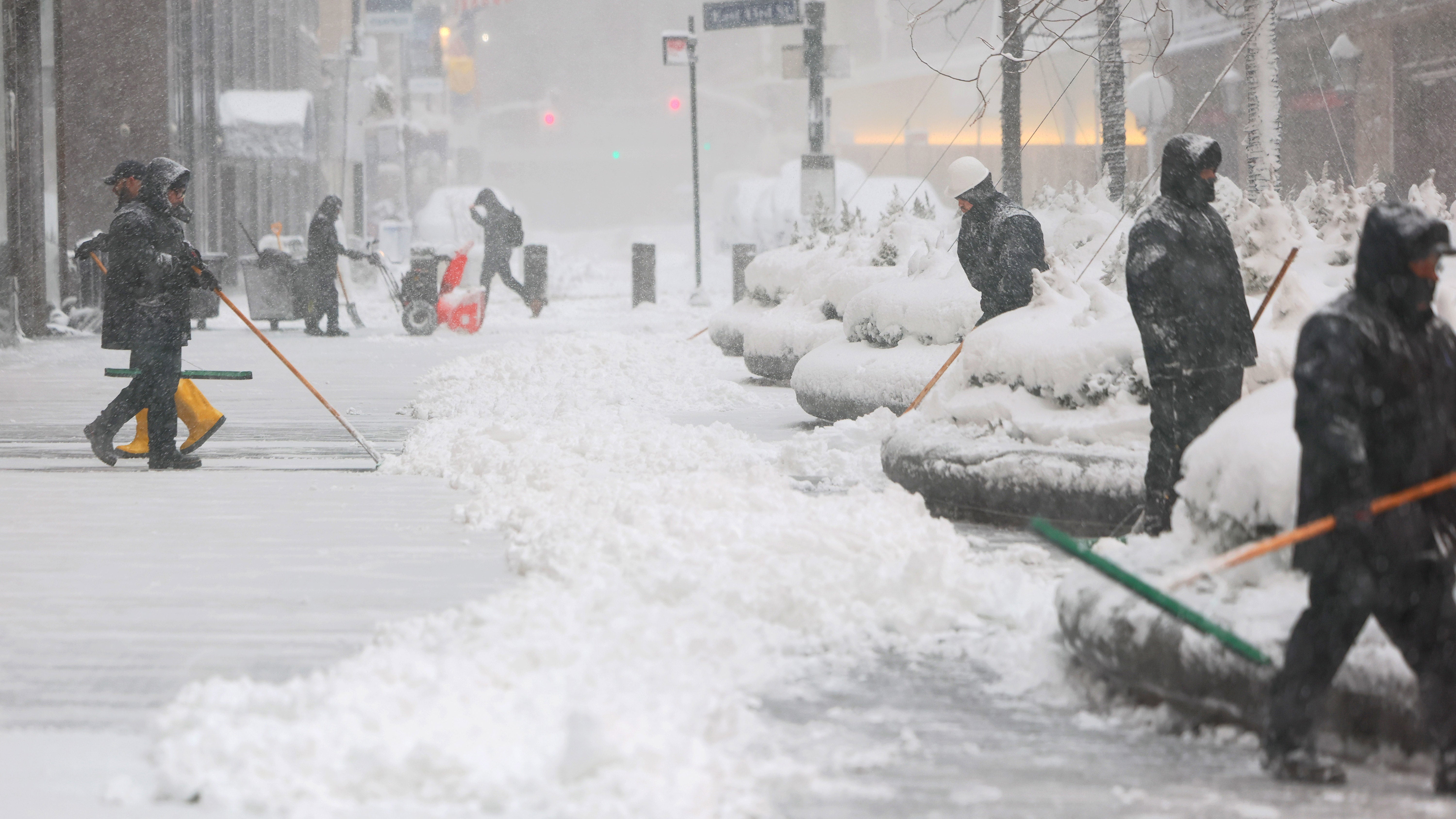 People shovel snow off a sidewalk near Grand Central Station in New York City amid heavy snow and strong winds from a blizzard.