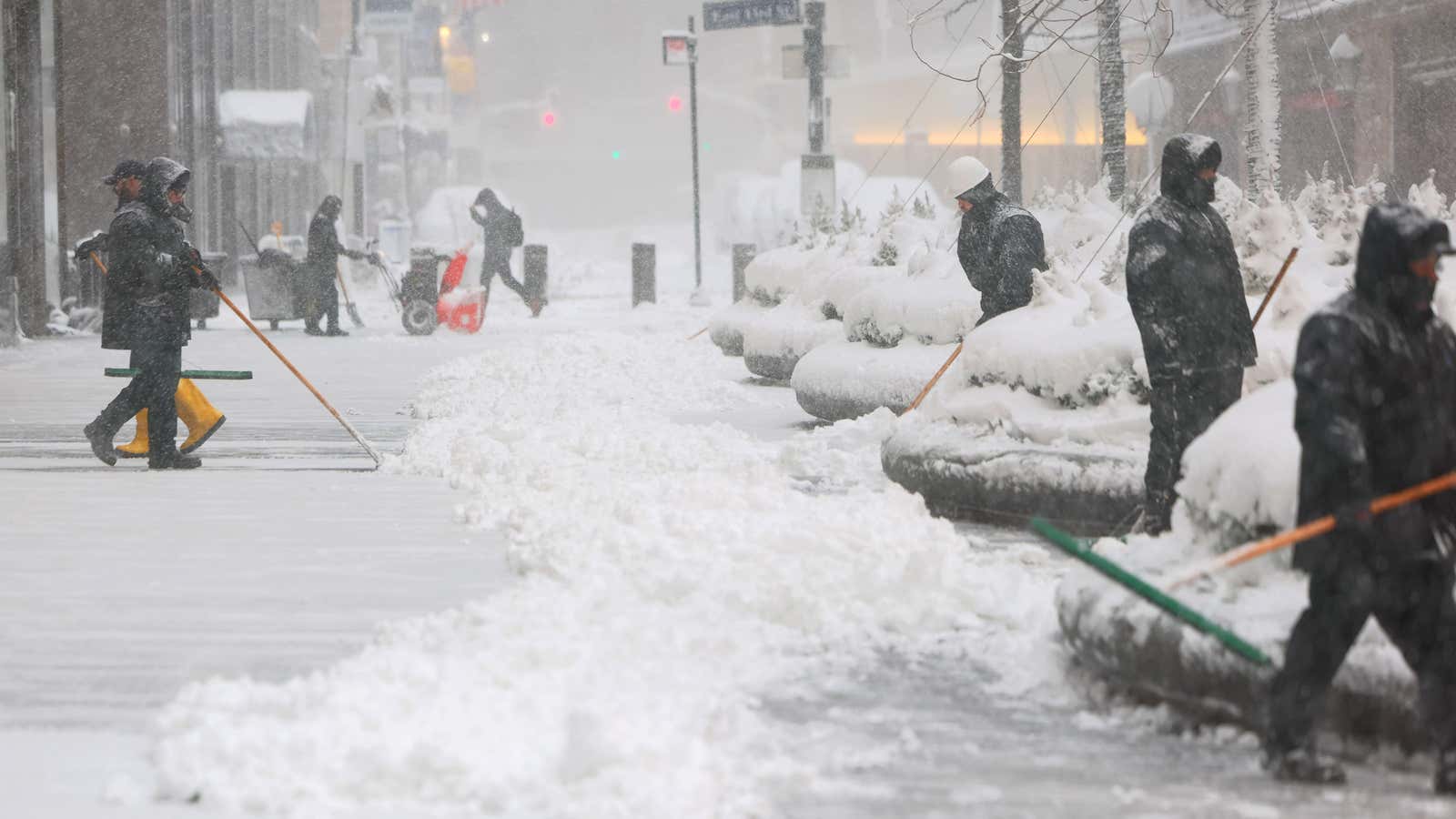 People shovel snow off a sidewalk near Grand Central Station in New York City amid heavy snow and strong winds from a blizzard.