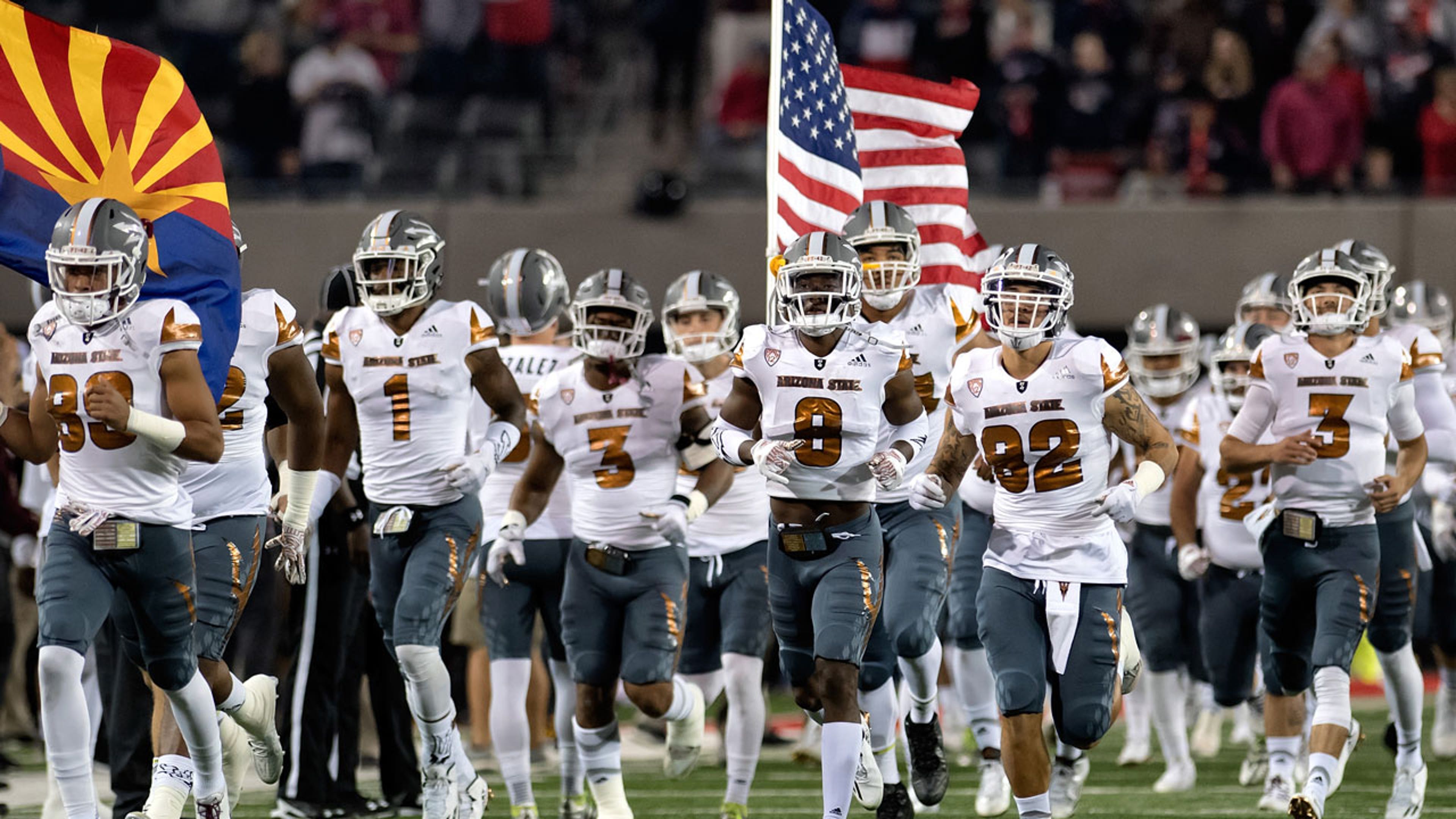 Football players run onto the field holding flags
