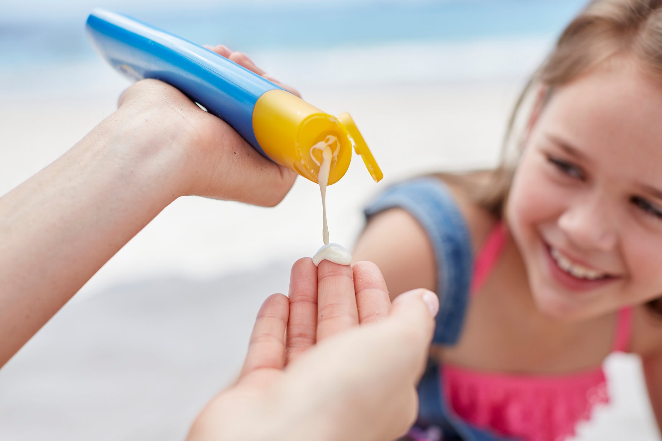Person applying sunscreen to girl at beach