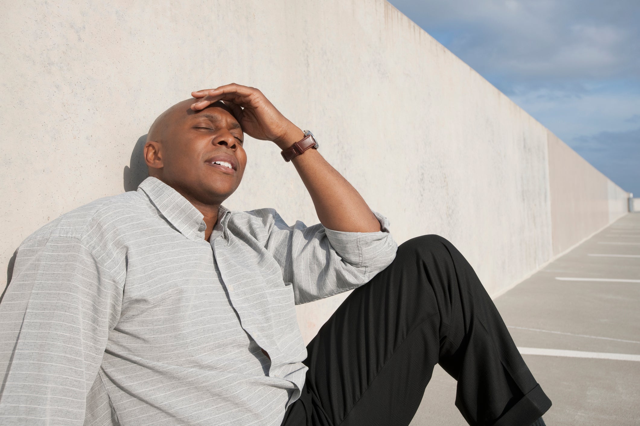 Man sitting and leaning against cement wall with migraine