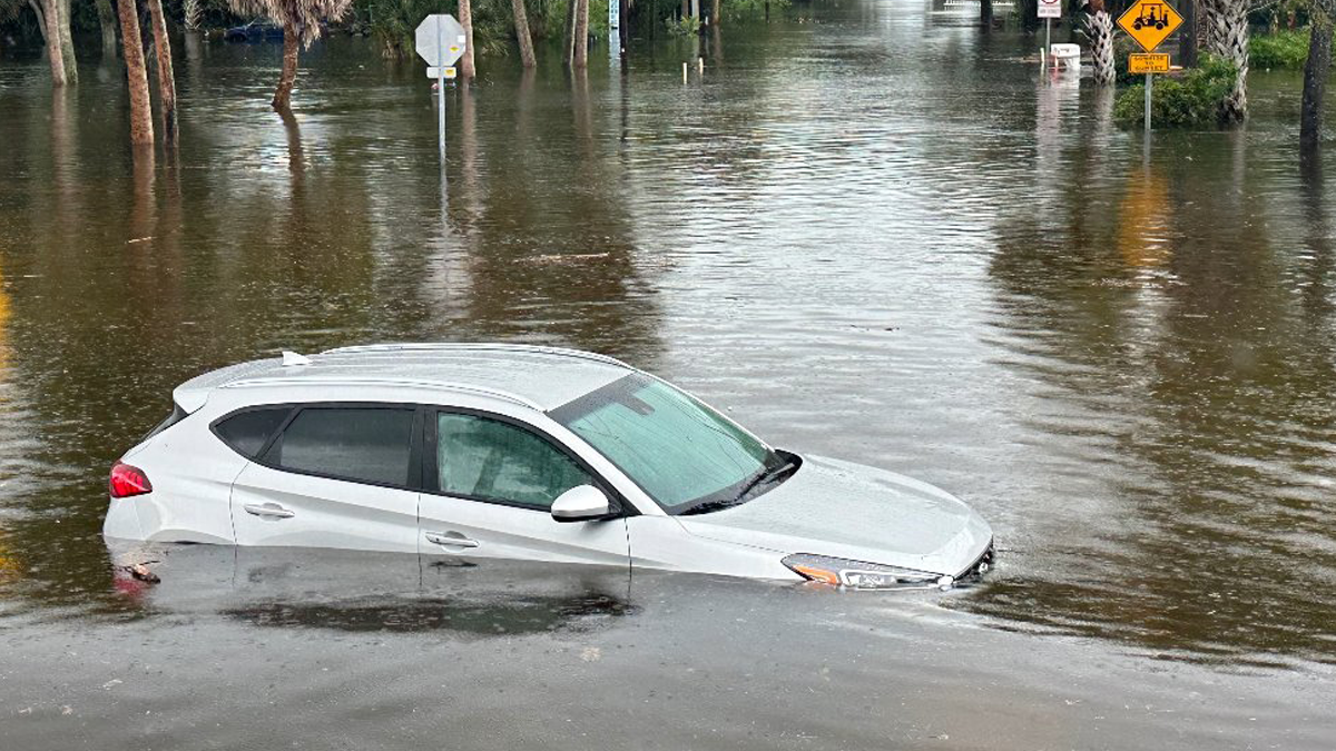 A white car is submerged in muddy water up to its windows.