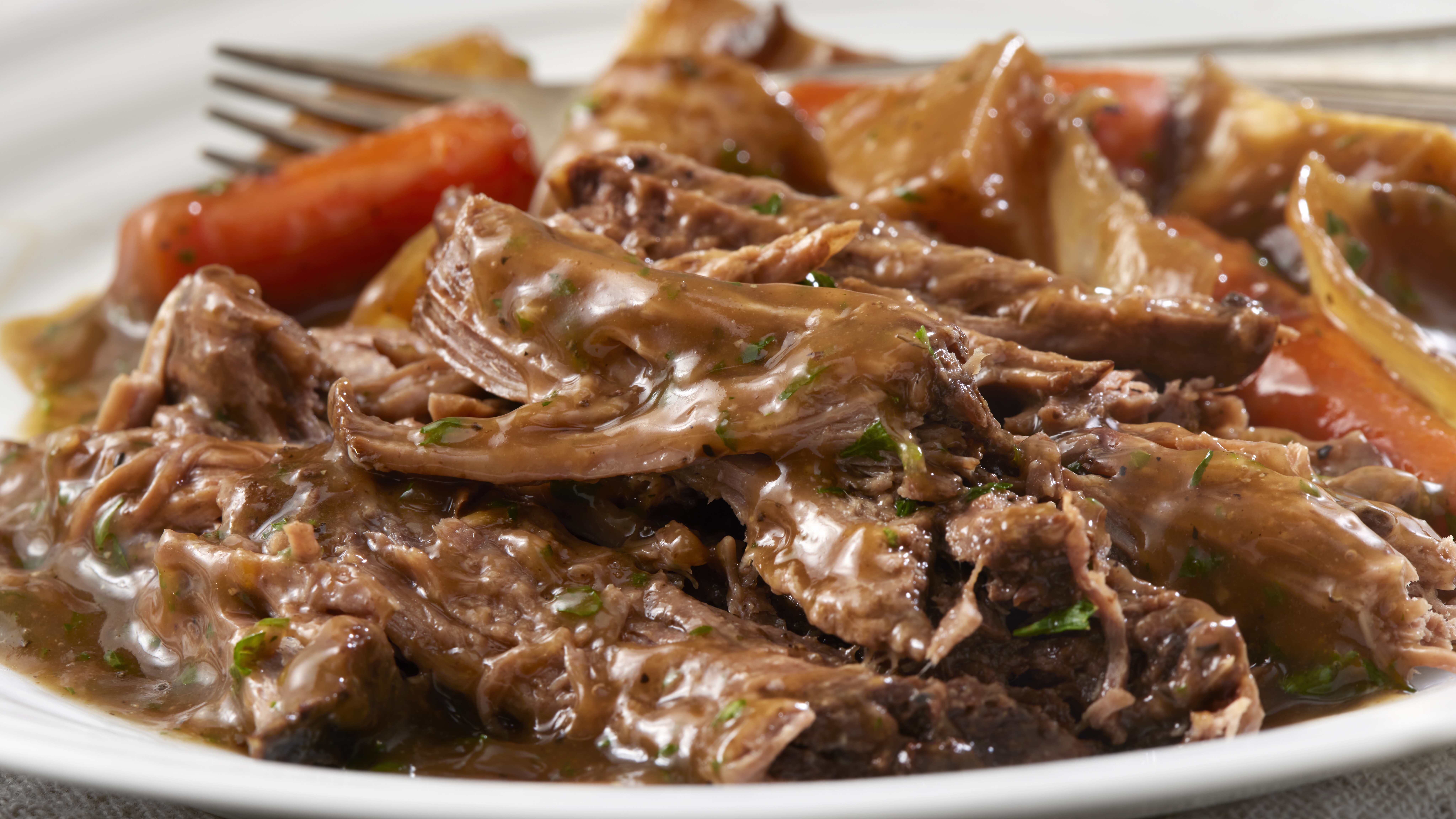 A plate is filled with chunks of meat and carrots covered in gravy. 