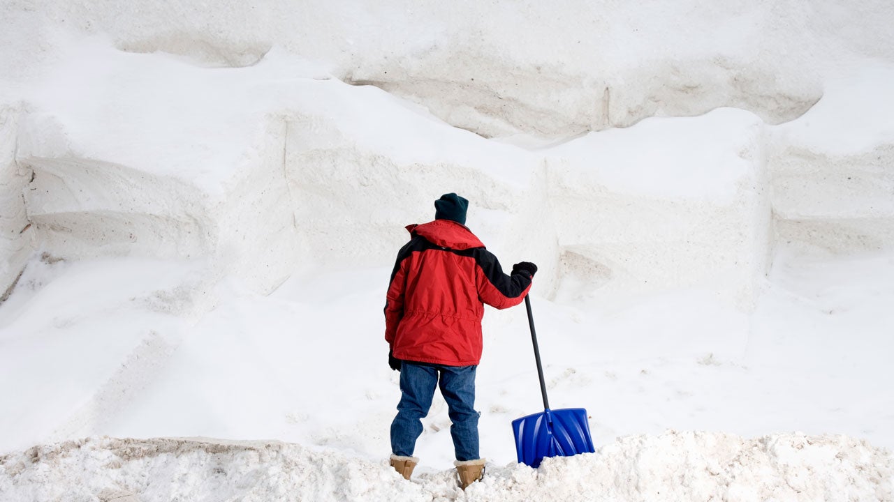 Wide shot of man in red jacket with shovel and snow