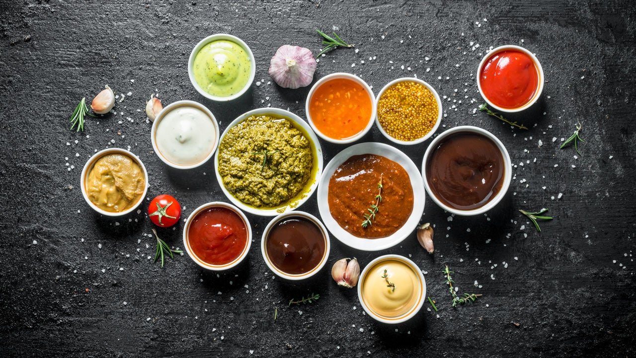 Set of sauces - tomato sauce, pesto, mustard, barbecue sauce, guacamole, mayonnaise on black rustic background