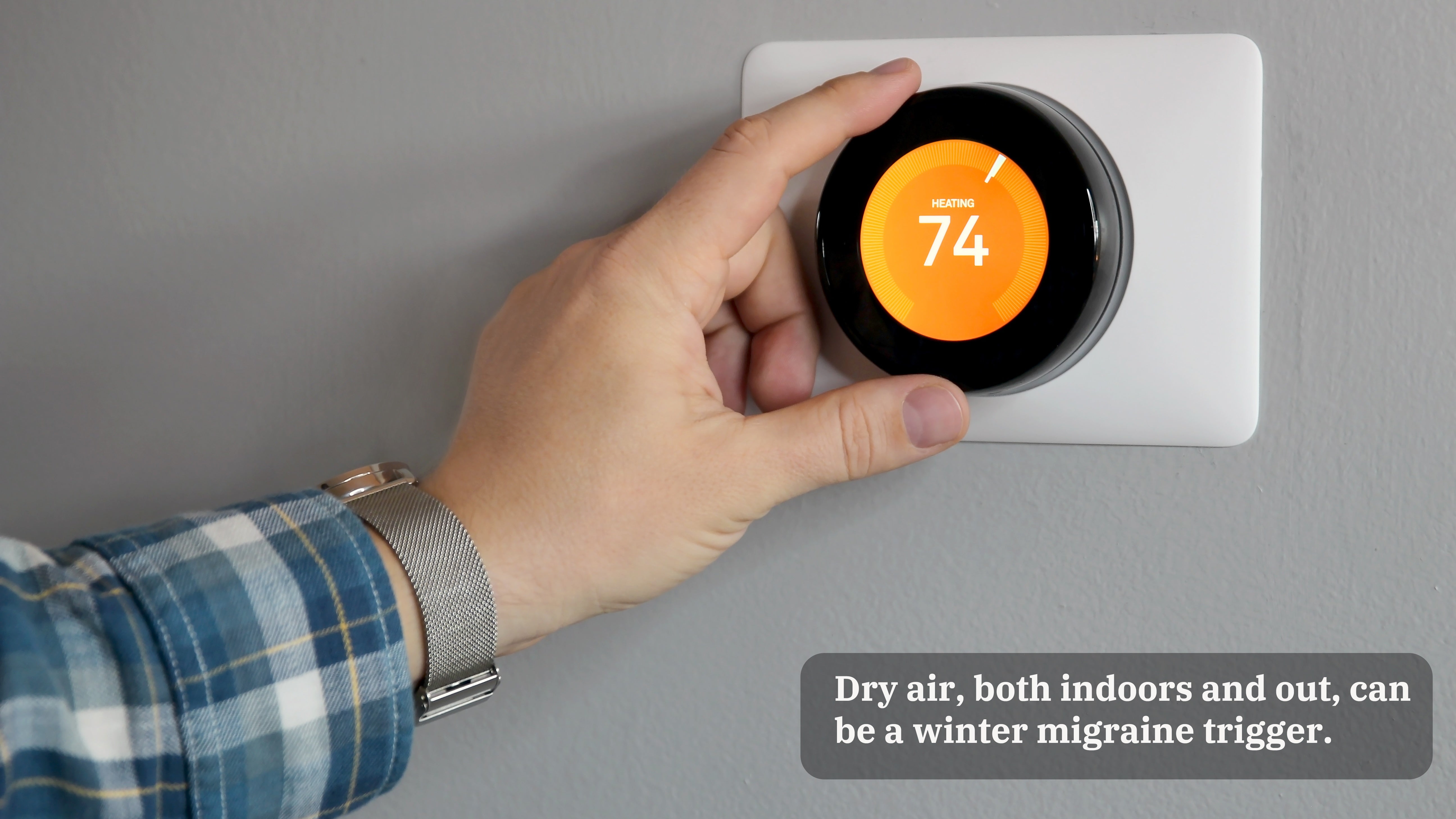 A hand adjusts a digital thermostat which reads "74 degrees" on an orange background. A caption on the image reads, "Dry air, both indoors and out, can be a winter migraine trigger."