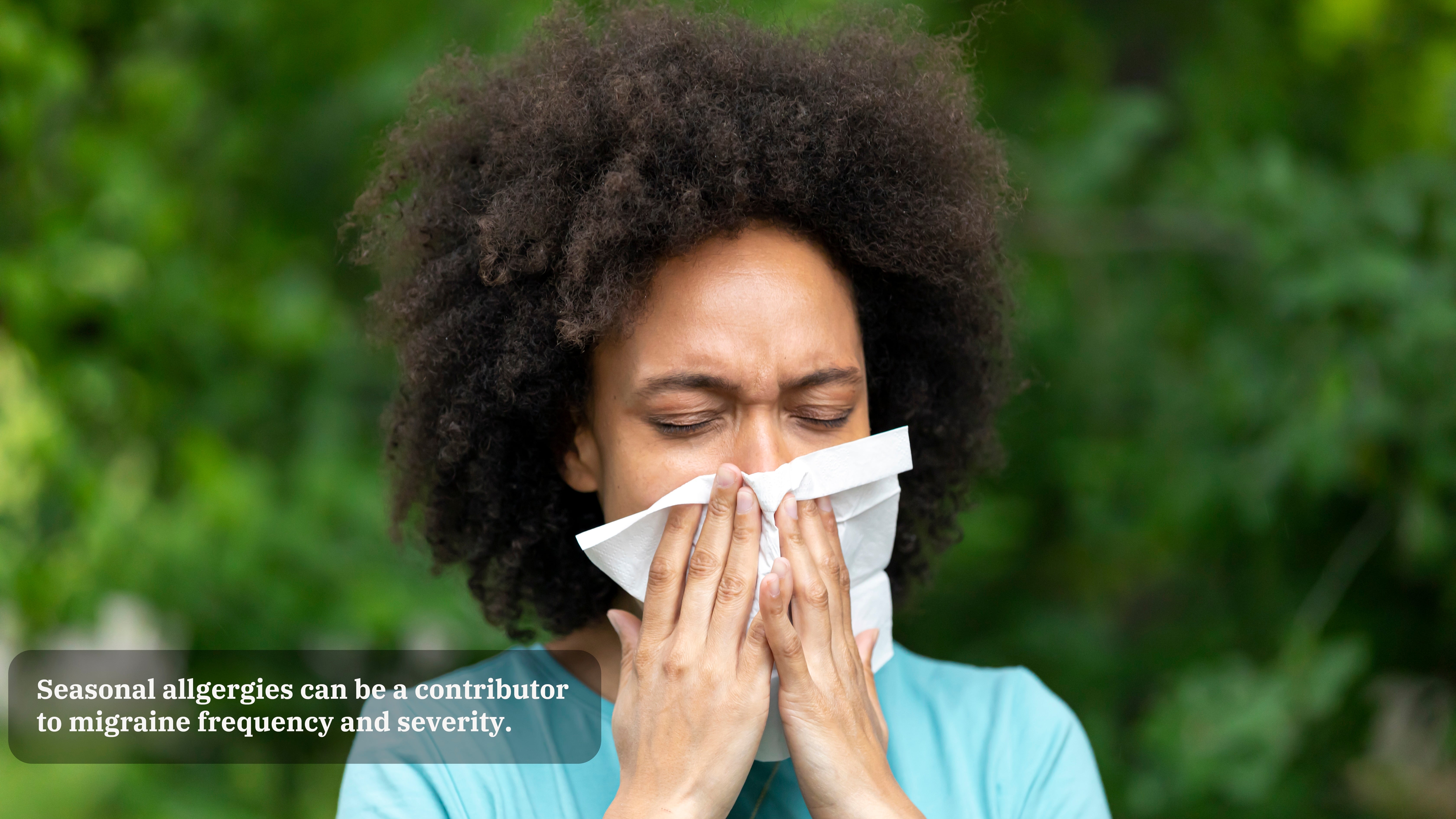 A woman in a light blue shirt blows her nose into a tissue in front of greenery. A caption on the image reads, "Seasonal allergies can be a contributor to migraine frequency and severity."