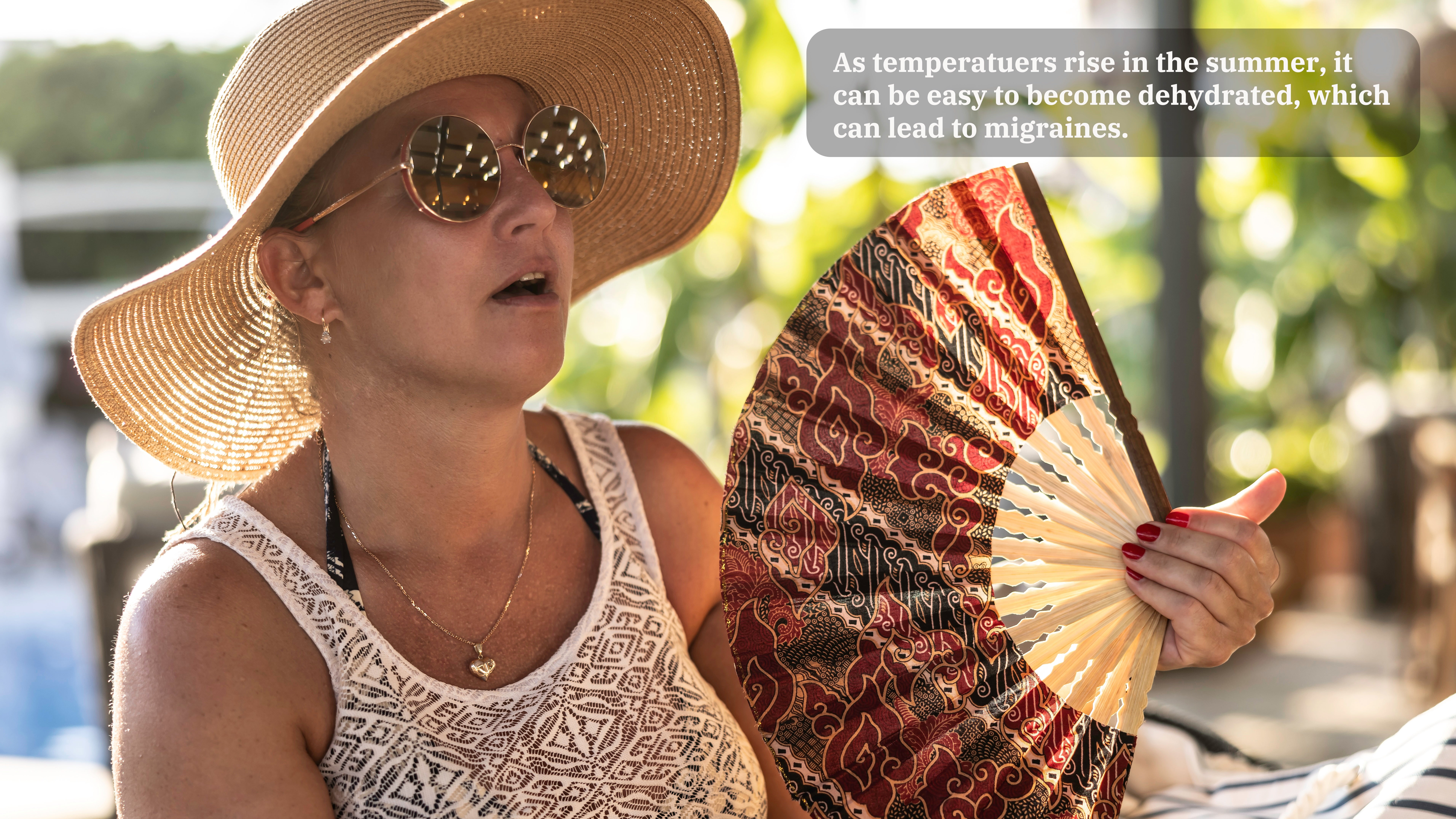 A woman in a hat and sunglasses and tank top cools herself using a handheld fan. A caption on the image reads, "As temperatures rise in the summer, it can be easy to become dehydrated, which can lead to migraines." 