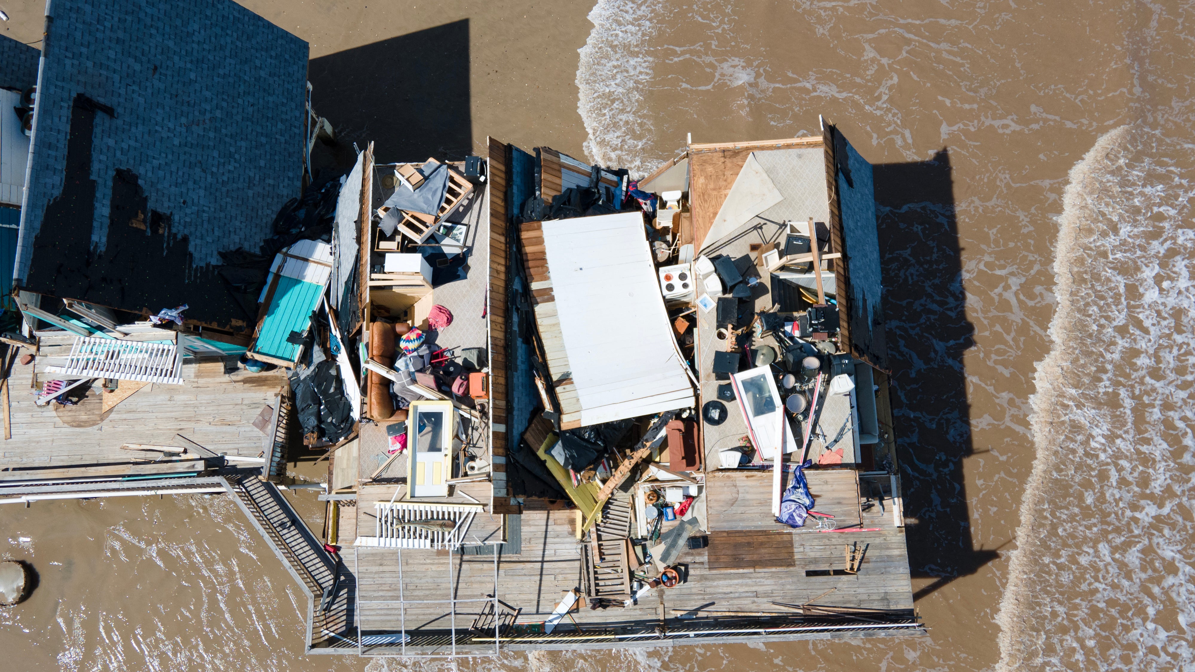 A leveled home is seen in an aerial view with surf creeping up.