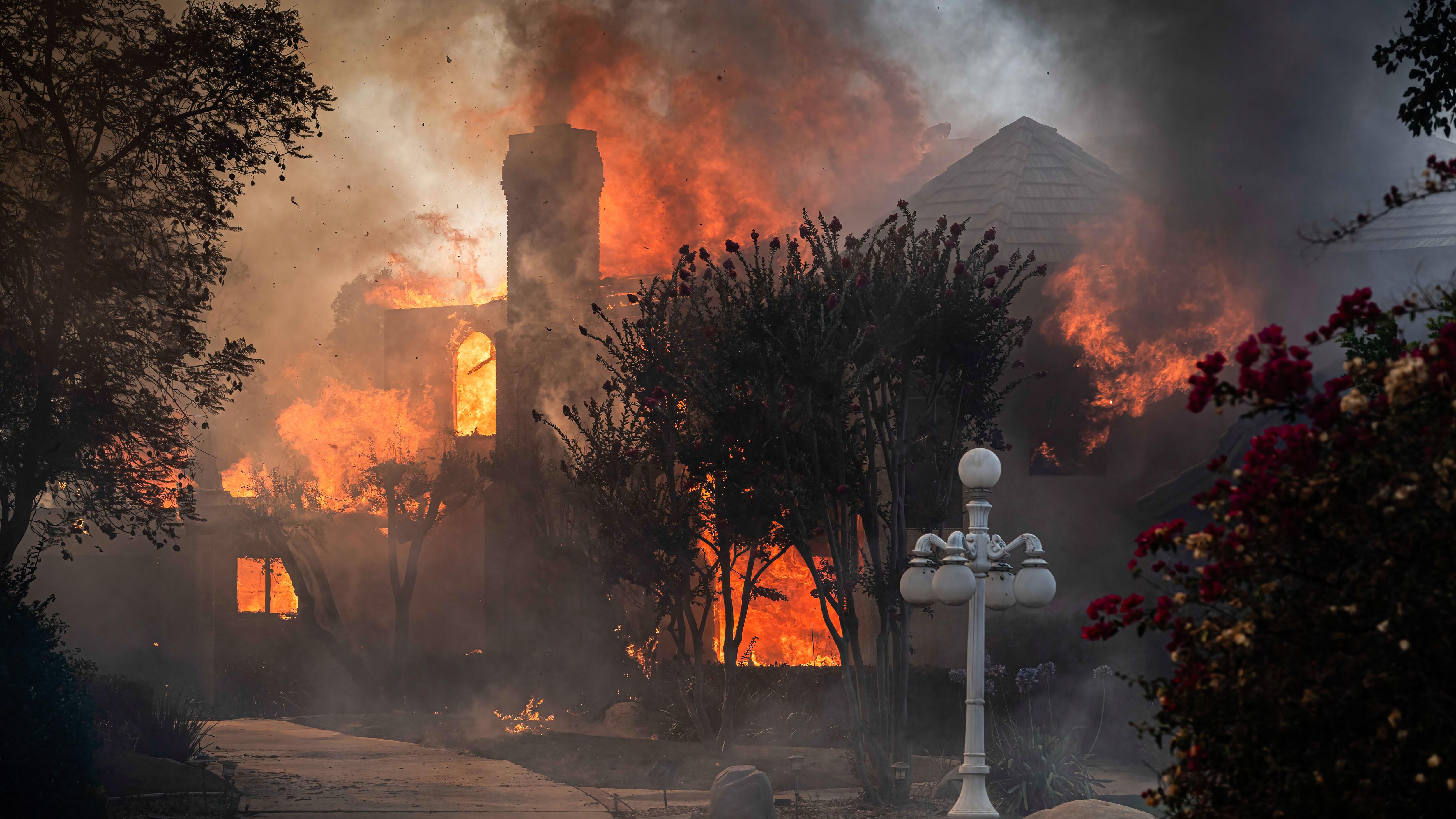 The orange glow of flames is seen through every window of a home, with smoke obscuring the view. 