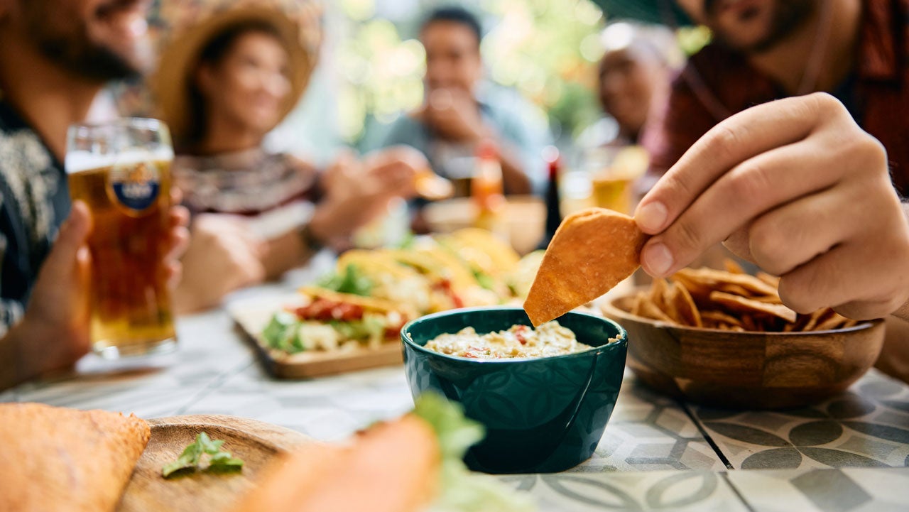 Close up of man dipping nacho chips in avocado dip while gathering with friends.